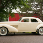 Cream-Colored Vintage Car in Snowy Landscape with Colorful Forest Background