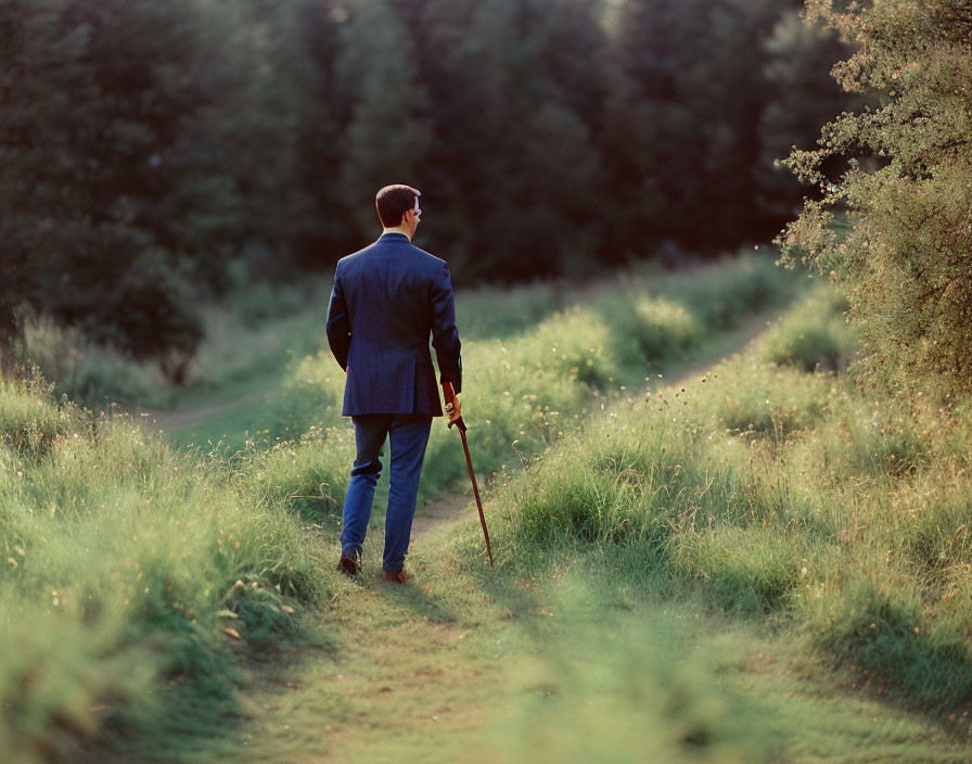 Man in suit with walking stick strolling on grassy path under sunlight.