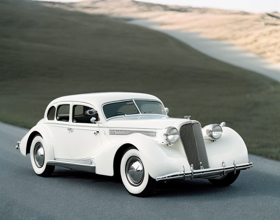 Vintage White Car with Front Grille on Smooth Road Amid Rolling Hills