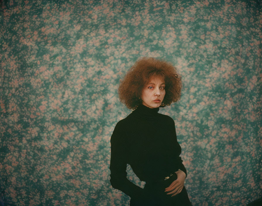 Curly haired woman in black turtleneck against floral backdrop