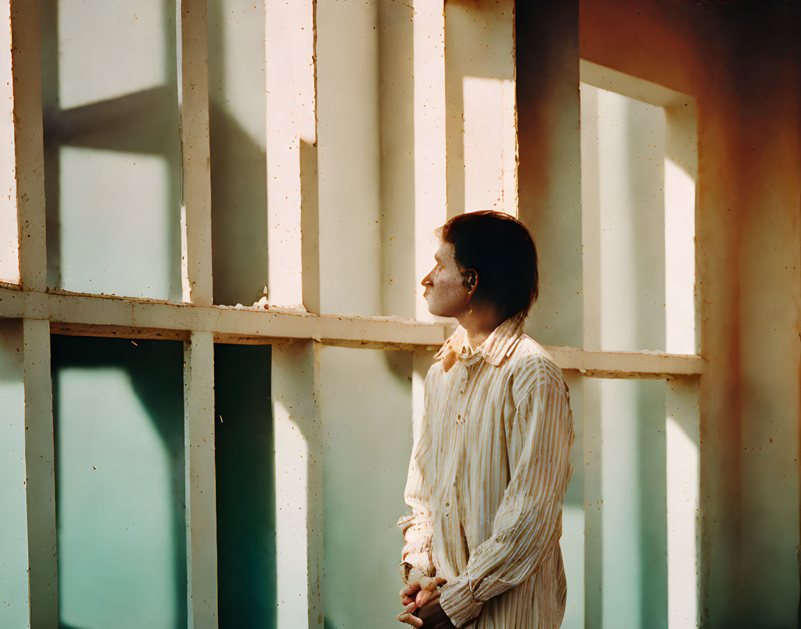 Person standing by window in warm sunlight with geometric shadows.