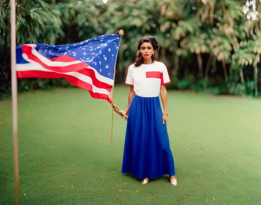 Woman in white top and blue skirt holding American flag on lush green grass