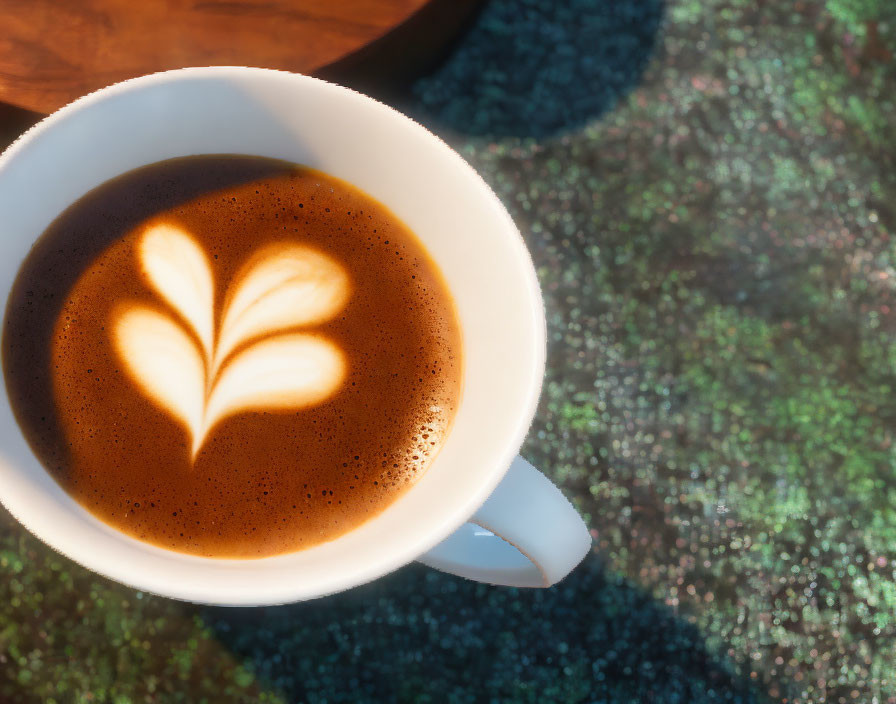 Latte art leaf on coffee cup on textured table in sunlight