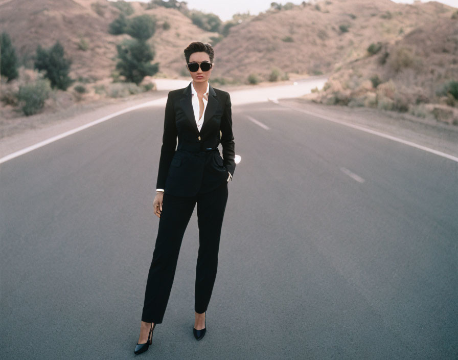 Person in Black Suit and Sunglasses Standing on Road Amid Hills