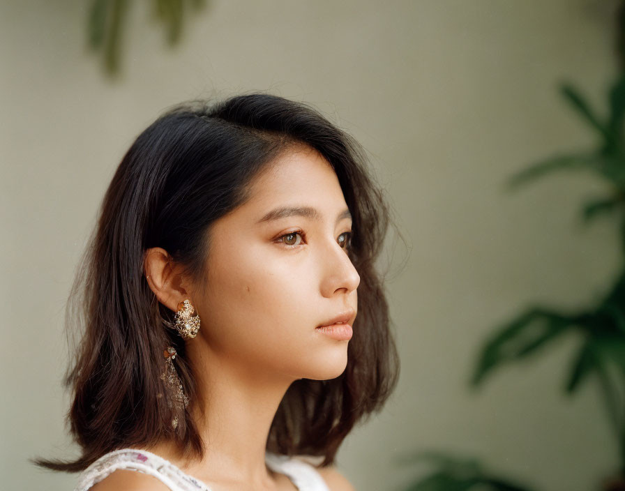 Dark-haired woman with intricate earring in side profile against soft background