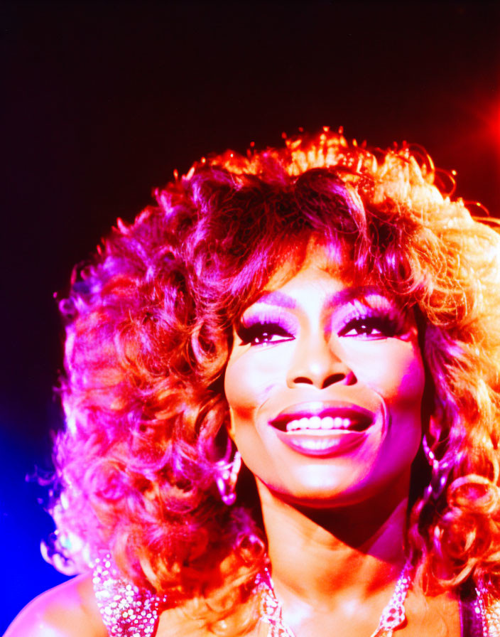 Colorful portrait of performer with curly hair, dazzling smile, and sparkly attire on purple background