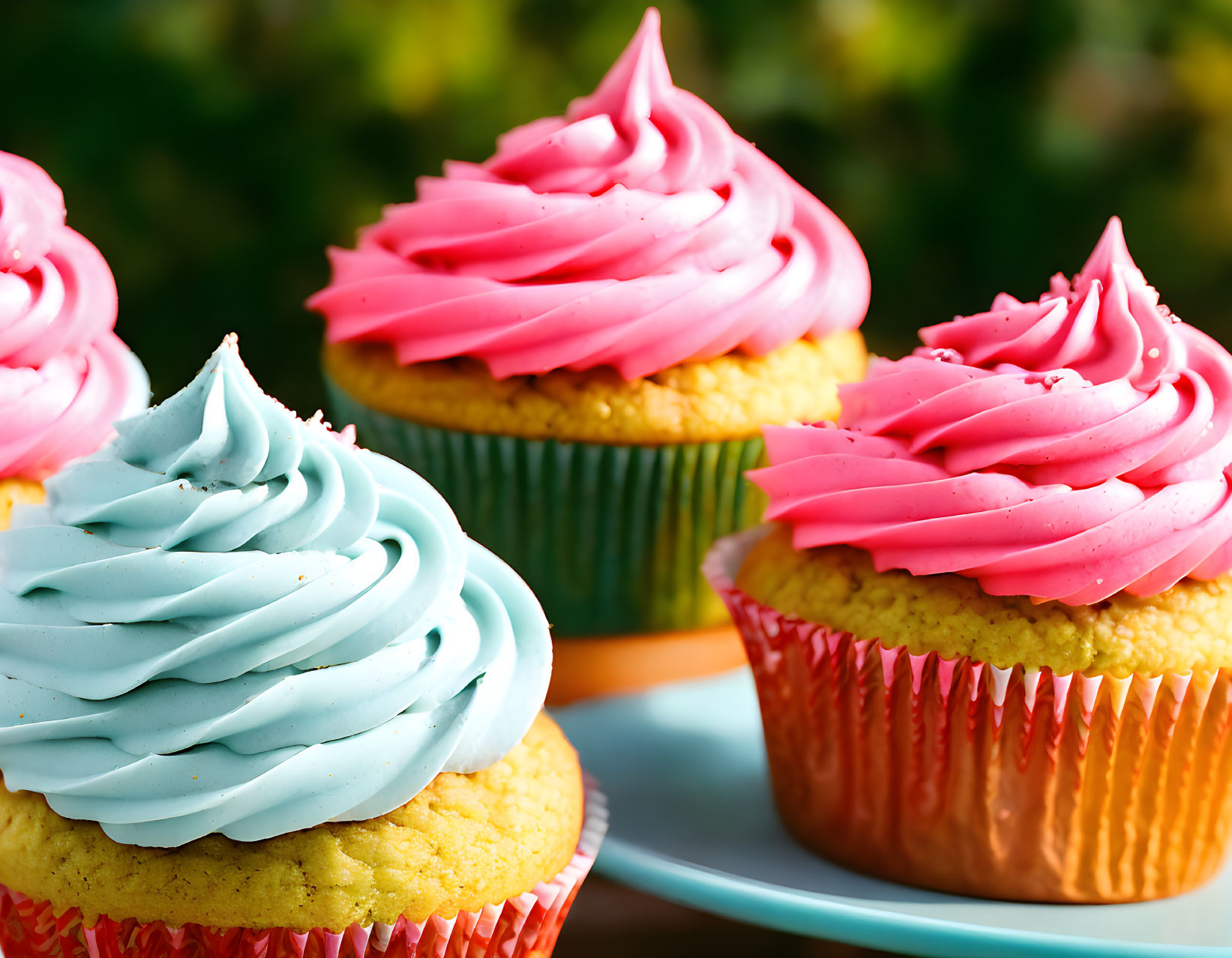 Four cupcakes with pink and blue swirl frosting on a plate