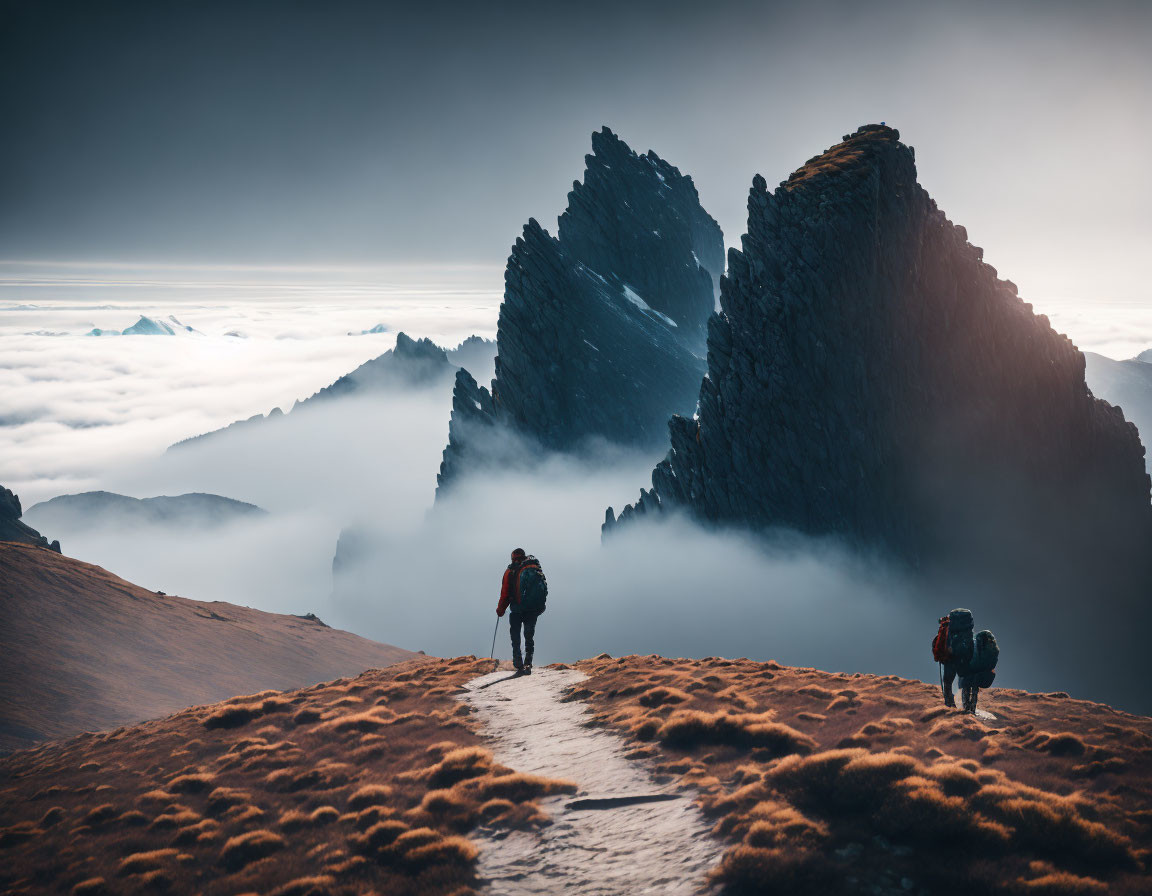 Hikers walking towards rugged mountain peak at misty sunrise