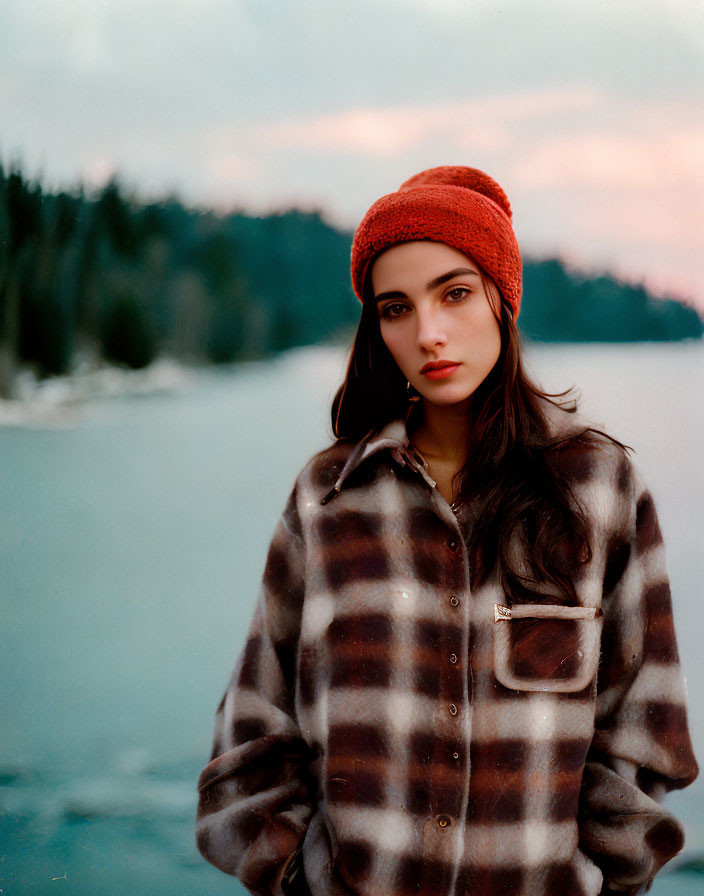 Woman in Checkered Coat and Orange Beanie by Lake and Forest at Dusk