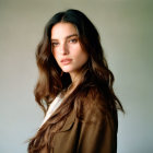 Portrait of woman with long brown hair and subtle expression in light blouse and brown jacket