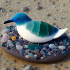 Bird-themed digital artwork featuring a sea glass mosaic body perched on a sandy shore nest.