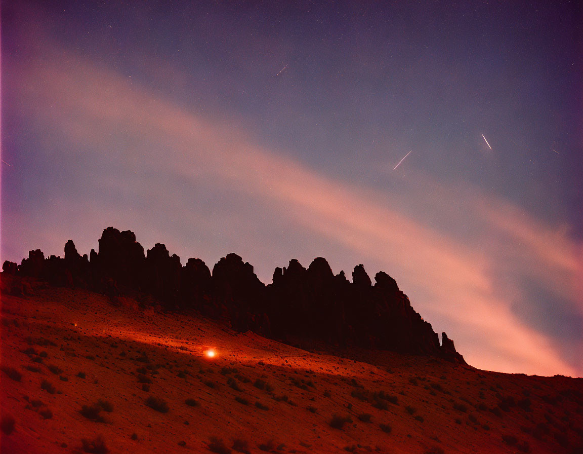 Reddish Night Sky with Streaking Stars and Glowing Light Over Jagged Mountains