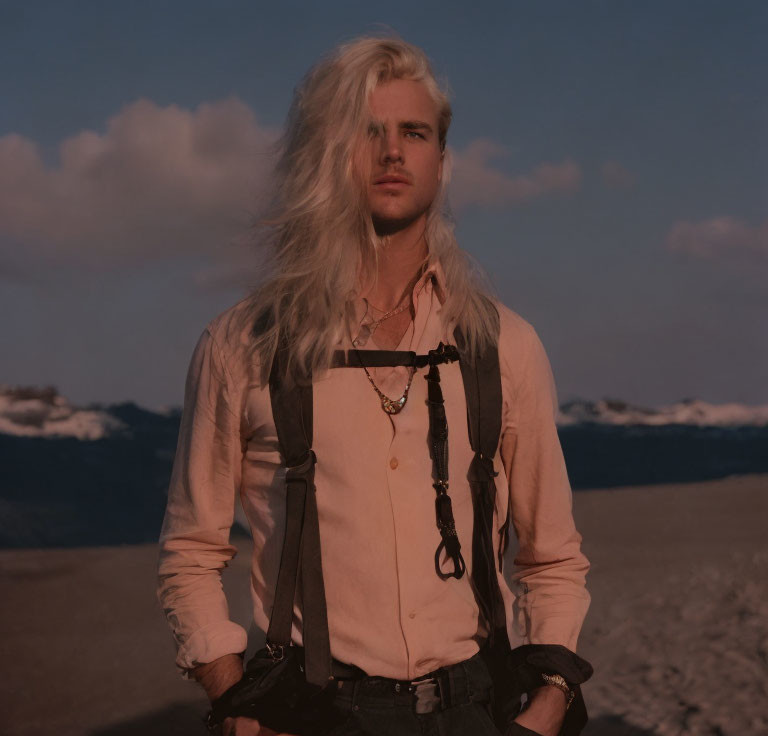 Blonde man in white shirt and suspenders in desert sunset landscape