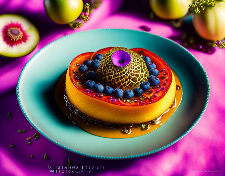 Colorful dessert on blue plate with blueberries, gold garnish, syrup drizzle, and fruity