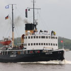 Vintage-style steamboat with two masts and black smokestack sailing on calm waters at sunset.