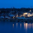 Twilight scene: Sailboats in calm harbor with glowing lights reflected on water