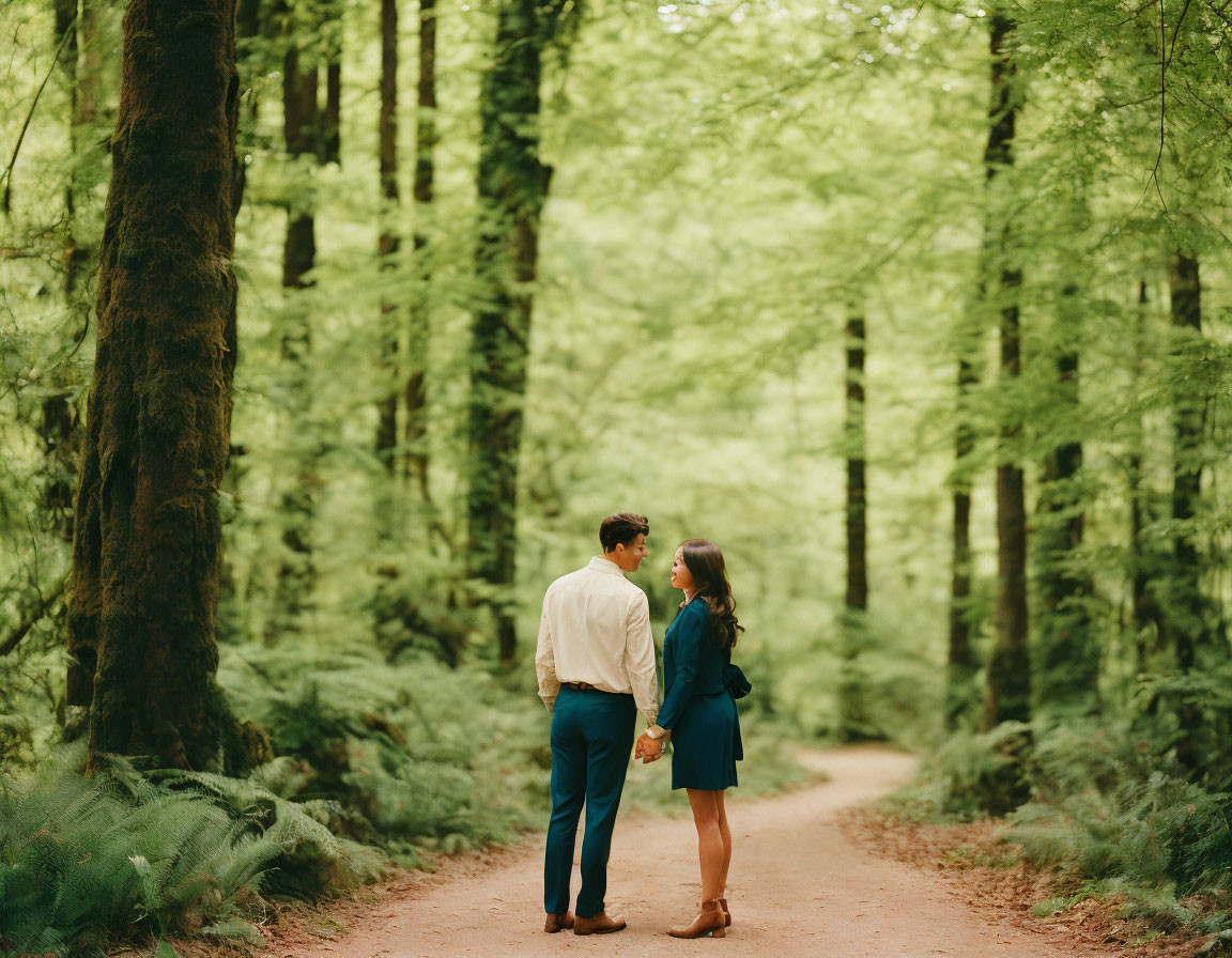 Couple holding hands in forest surrounded by tall green trees