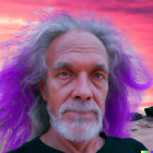 Elderly man with gray curly hair in front of pink and purple sunset