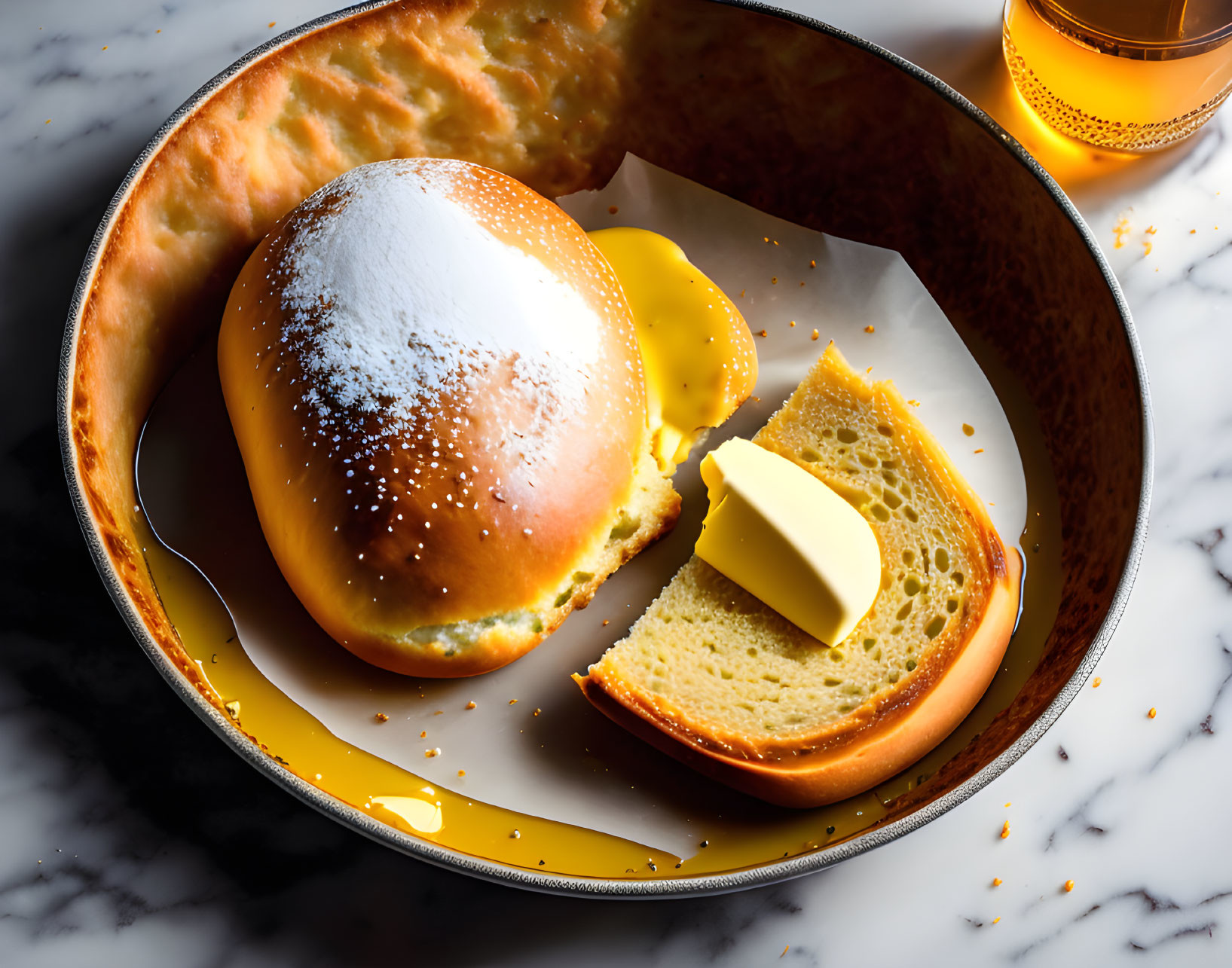 Golden-brown bread roll with butter and honey in round dish