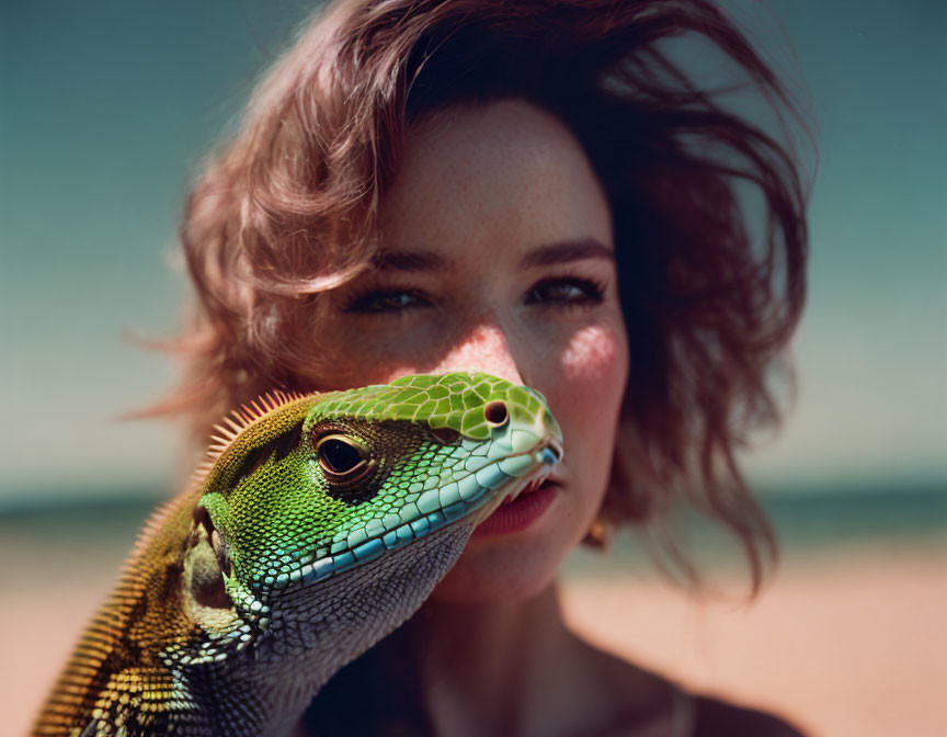 Woman with wind-tousled hair and bright eyes close-up with vivid green iguana outdoors under