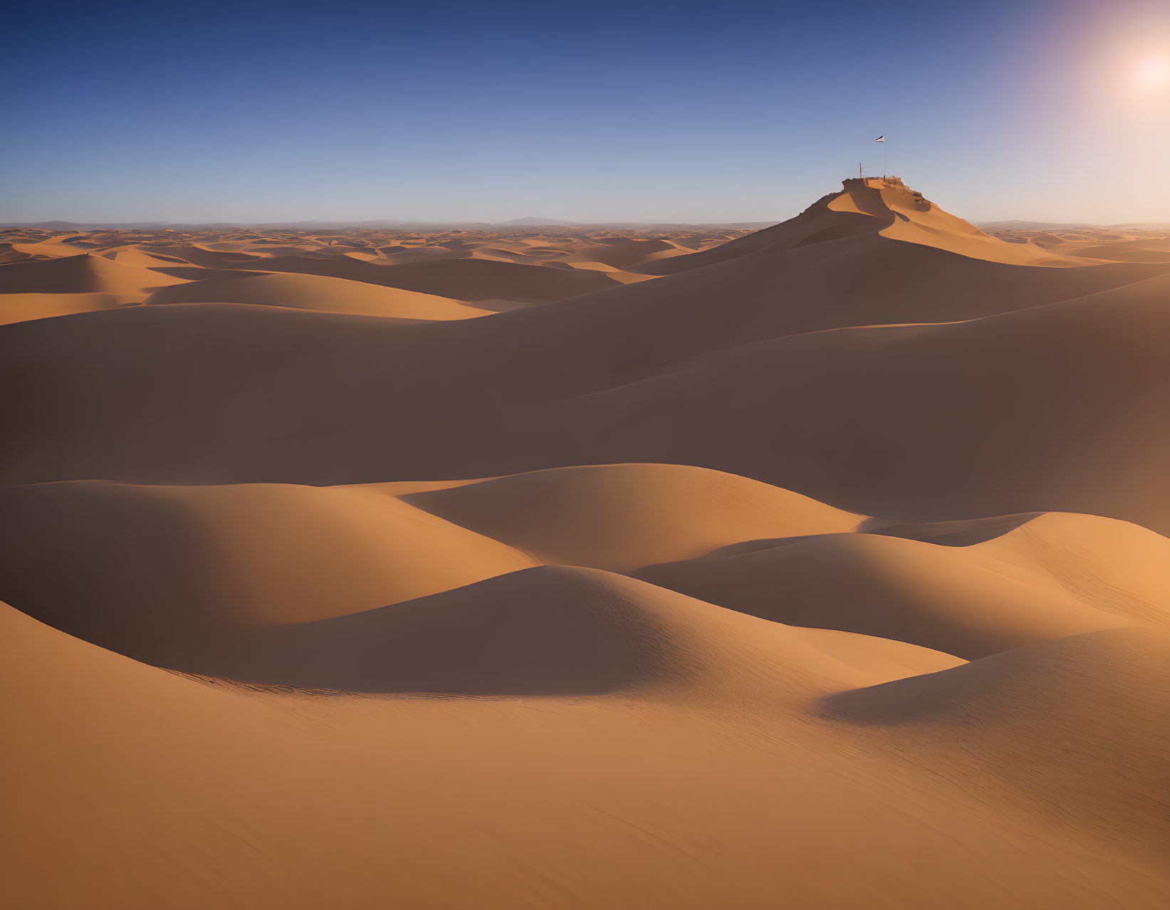 Vast desert dunes under clear sky with flag on distant peak