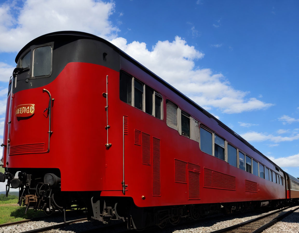 Vintage red train carriage on tracks under blue sky with clouds.