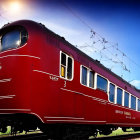 Vintage red train carriage on tracks under blue sky with clouds.