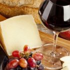 Assorted Cheese Wheels, Slices, Grapes, and Red Wine on Wooden Board