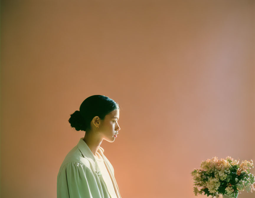 Serene woman with flowers in natural light on peach backdrop