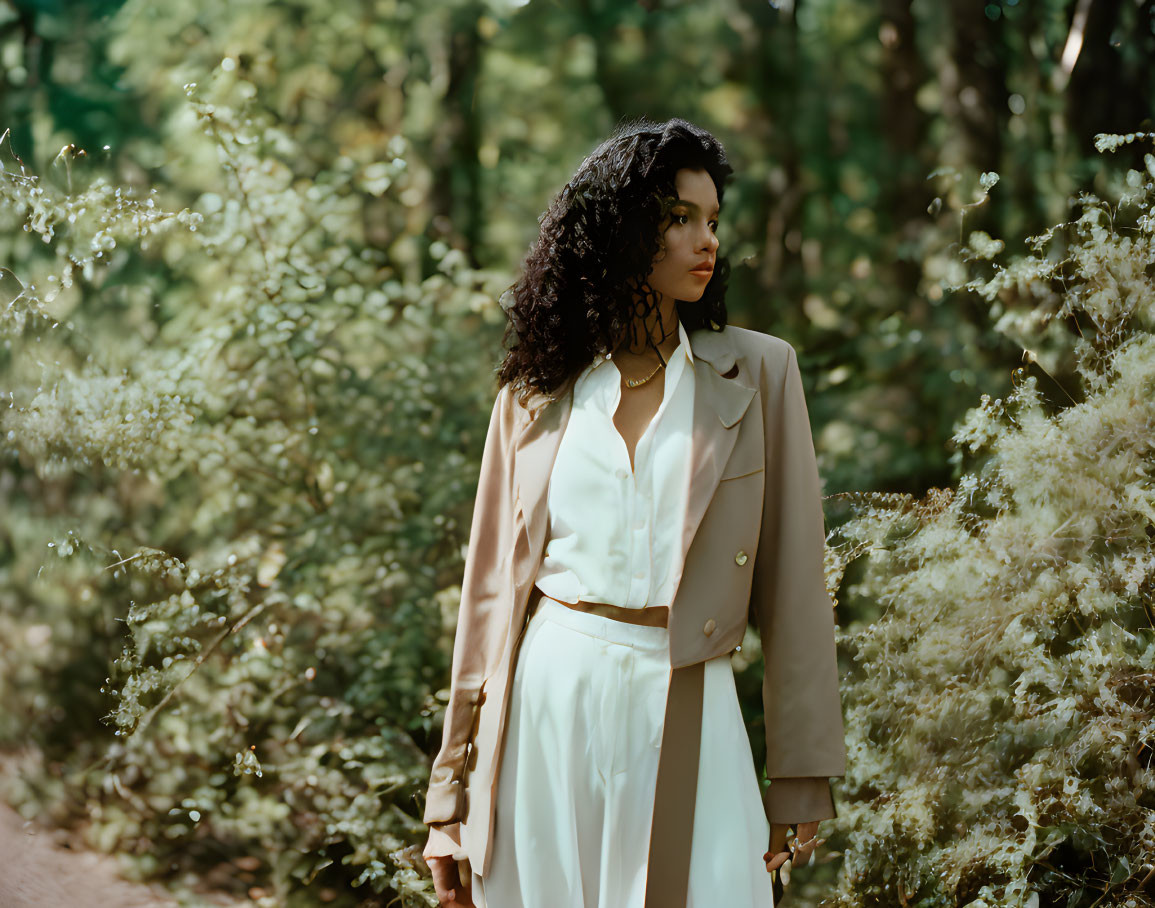 Curly-Haired Woman in Chic Trench Coat Amid Green Foliage