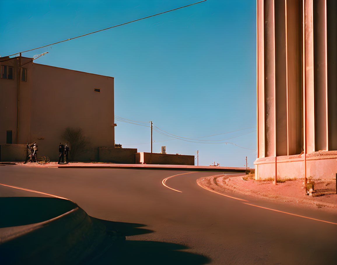 Curved road in quiet area with buildings and pillars under clear blue sky