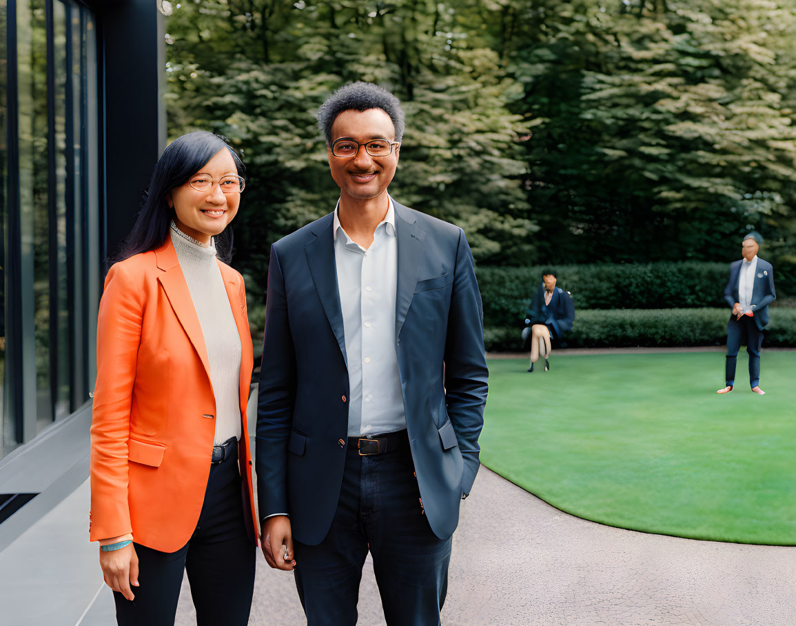 Professional woman in orange blazer and man in suit standing confidently outdoors.