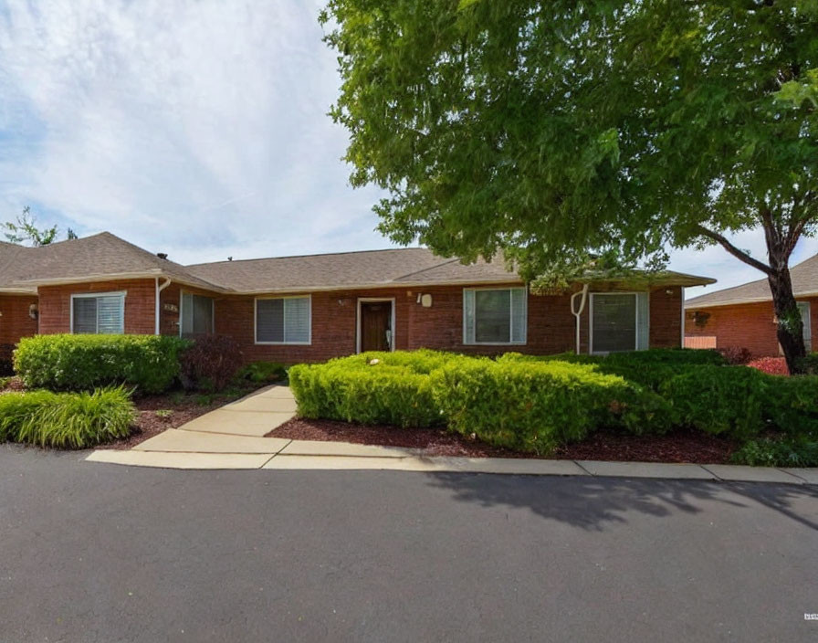 Brick house with manicured lawn, tree, and walkway under blue sky