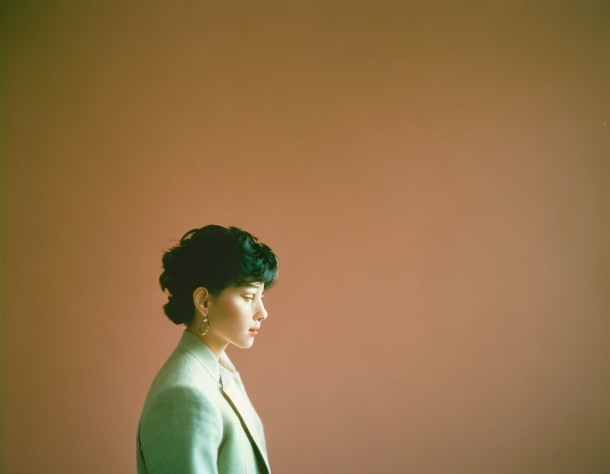 Profile view of person with short hair in green blazer on orange backdrop