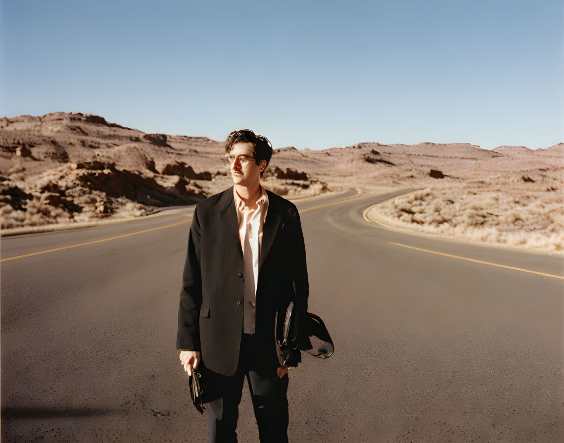 Man in dark suit on desert road holding helmet with rocky background