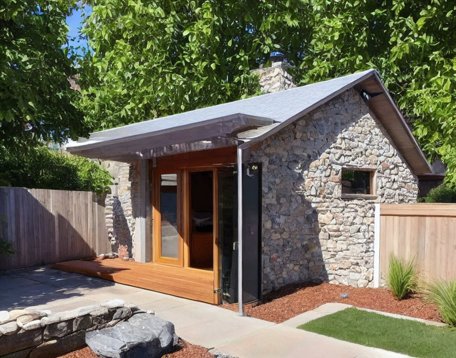 Stone cottage with modern wooden door in manicured lawn & wooden fence under blue sky