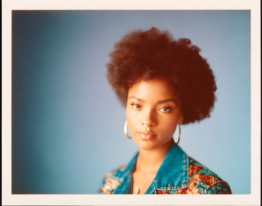 Woman with Afro Hairstyle in Denim Jacket and Hoop Earrings against Blue Background