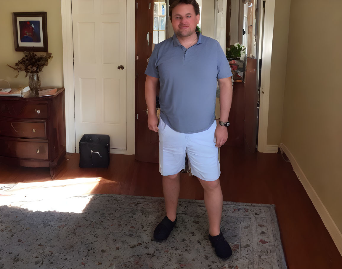 Man in blue polo shirt and white shorts smiling in sunlit room