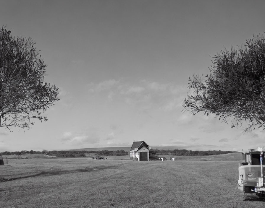 Monochrome rural landscape with house, trees, sky, and vehicle.