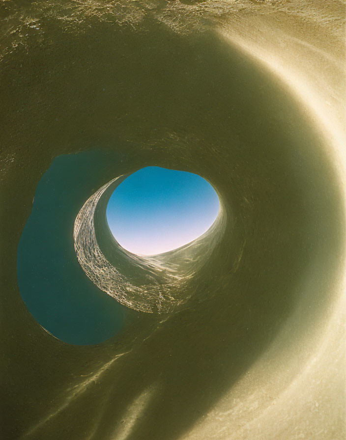 Sandy cylindrical pit with smooth walls and round opening to clear blue sky