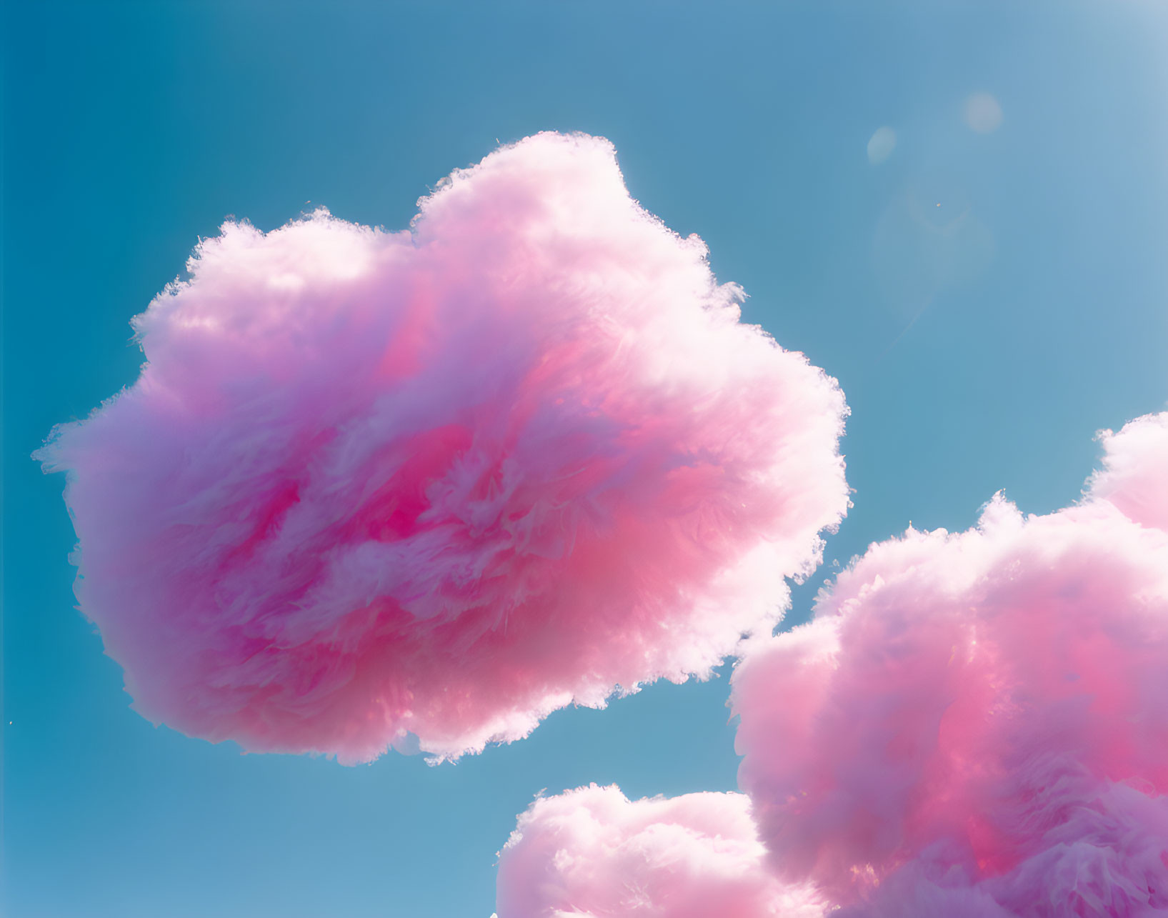 Pink fluffy clouds in bright blue sky with soft sunlight.