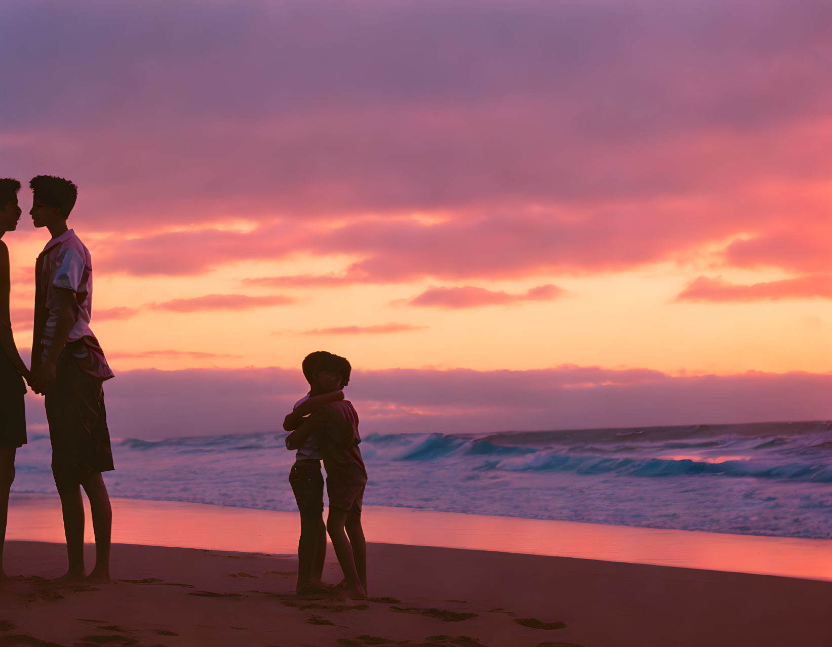 Two people on beach at sunset with vibrant sky & waves