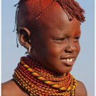 Dark-skinned woman in pink beanie and orange scarf with freckles and gold earrings.