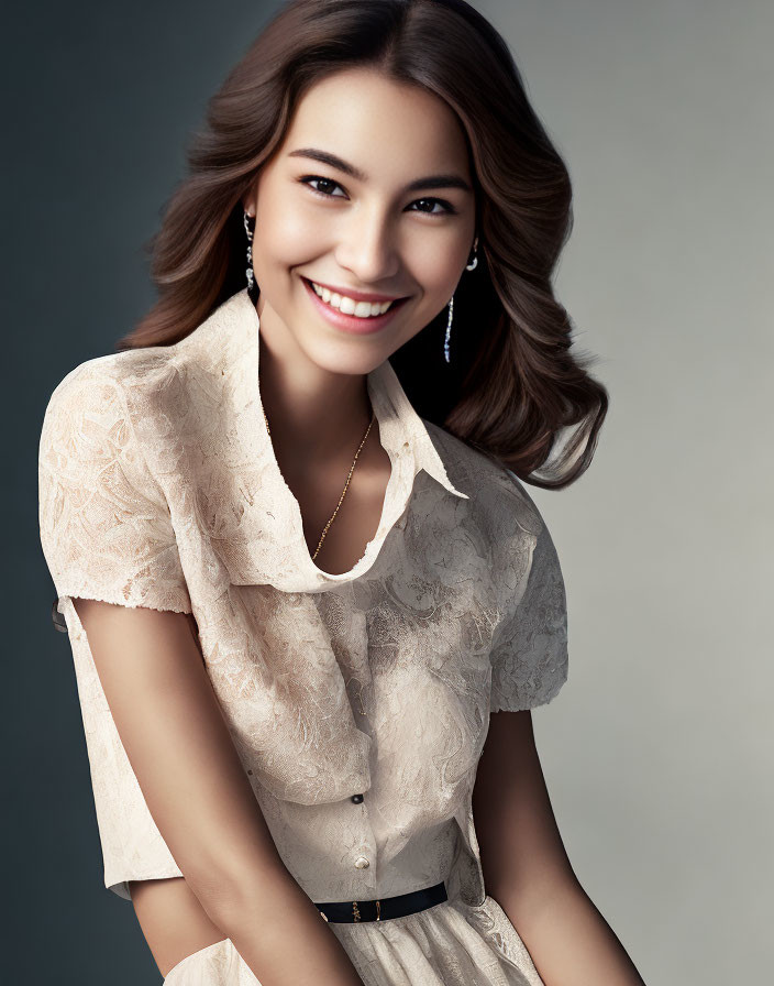 Smiling woman with wavy brown hair in lace blouse on grey background