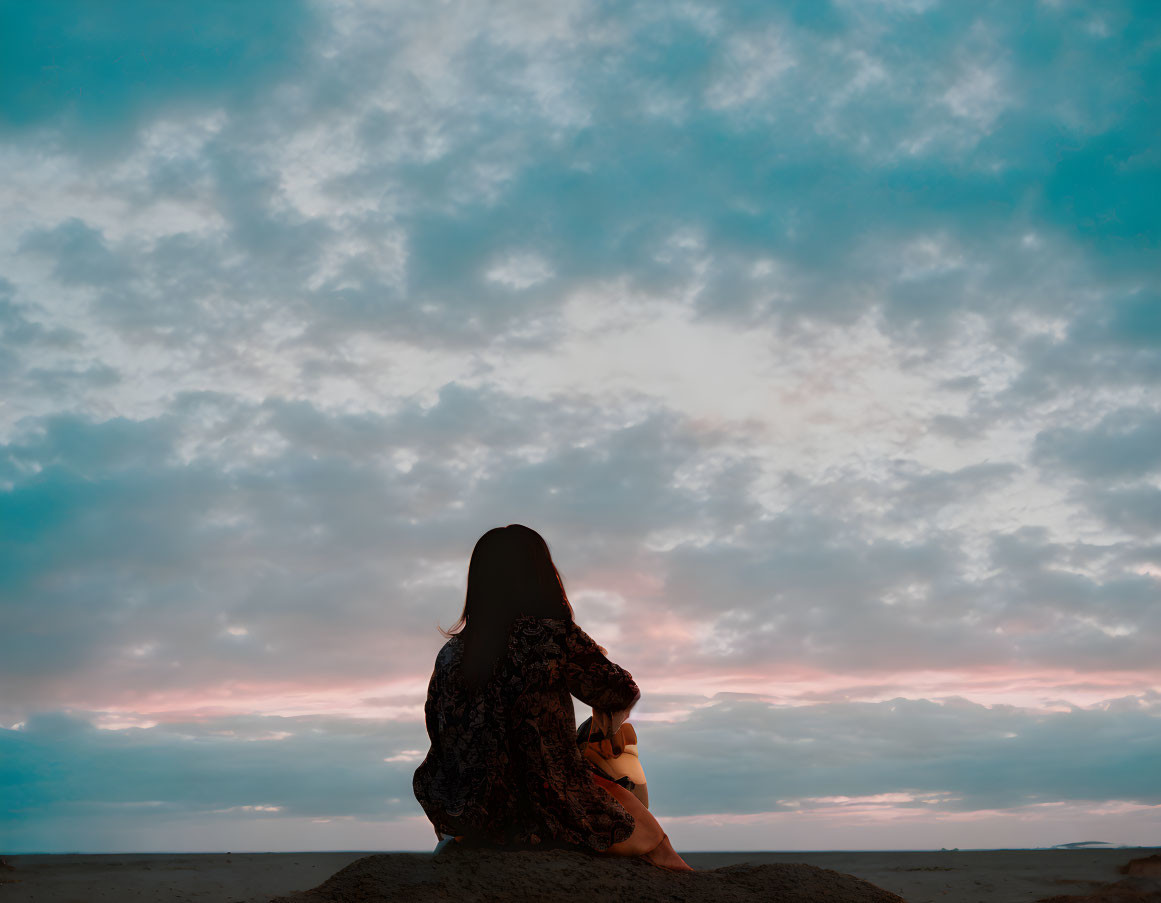 Silhouette of person gazing at blue and orange sky at dusk or dawn