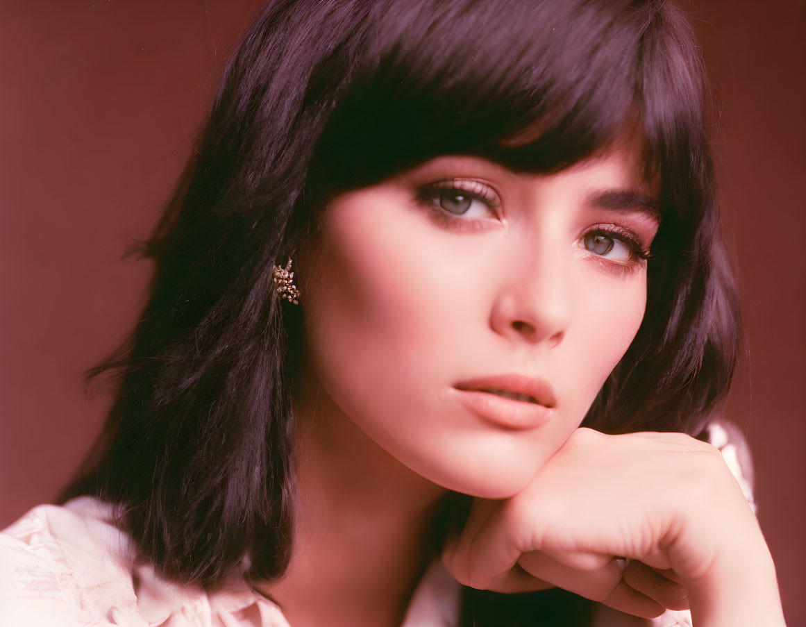 Dark-haired woman with bangs in light blouse and star earring