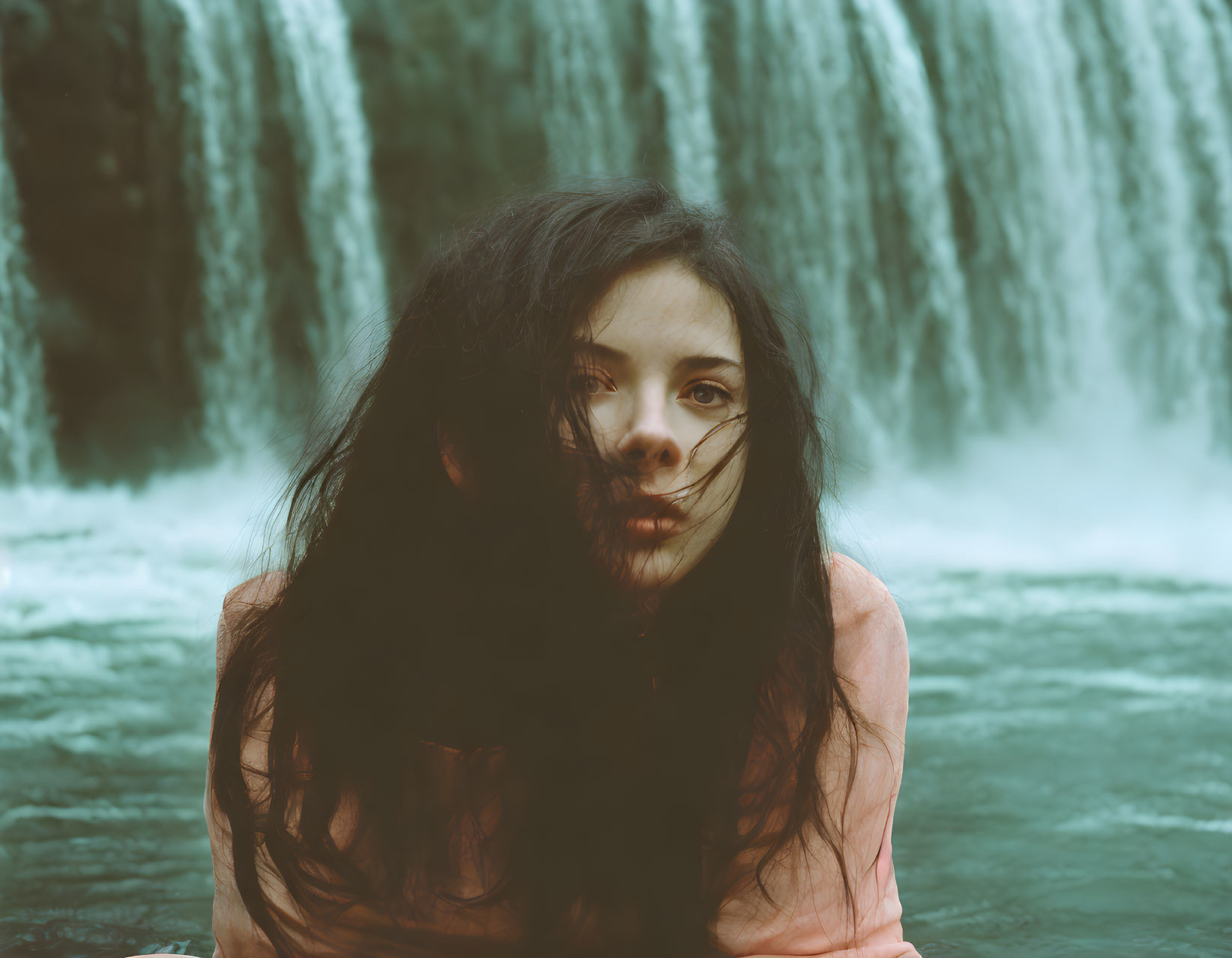 Woman with loose hair gazing at cascading waterfall