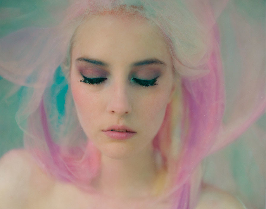 Pale-skinned woman with dramatic makeup enveloped in pastel fabric