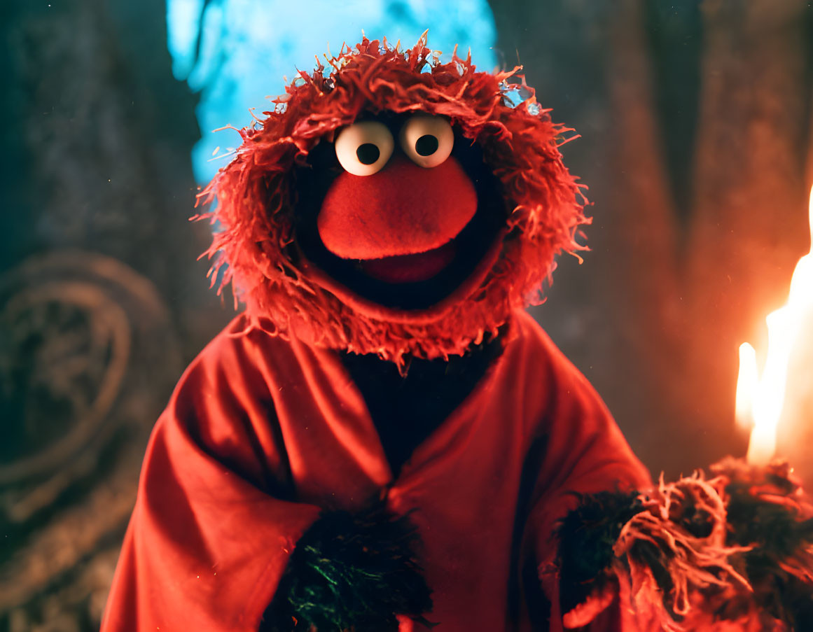 Red furry puppet with orange nose and robe in front of warm candlelit background