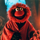 Red furry puppet with orange nose and robe in front of warm candlelit background